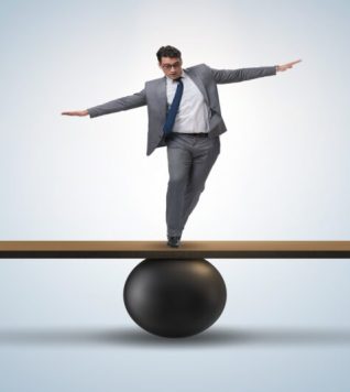 Businessman trying to balance on ball and seesaw